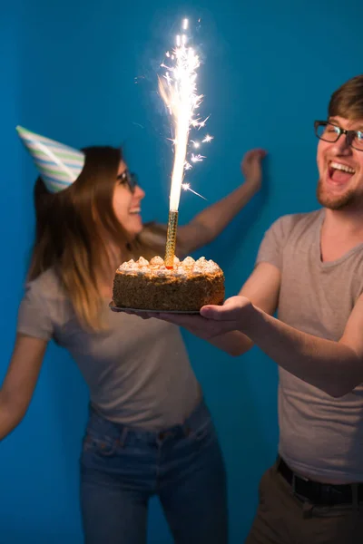 재미 괴상한 남자와 여자는 파란색 배경위에 촛불과 생일 케이크를 들고 휴일 모자와 안경을 착용 — 스톡 사진