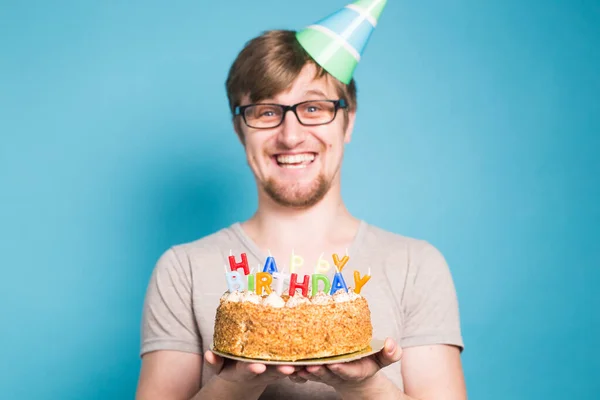 グリーティングペーパーの帽子をかぶった面白いクレイジーな若者は、お祝いのケーキの一部をかみつけたいと思っています。周りをだまし、誕生日の挨拶の概念。スペースのコピー — ストック写真