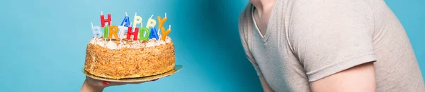 Hands holding a birthday cake with candles and the inscription birthday on a blue background. Copy Space