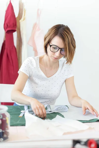 Молодая симпатичная студентка учится у дизайнера одежды в колледже и делает свою первую диссертацию, сидя за столом с швейной машинкой. Концепция дизайна одежды . — стоковое фото
