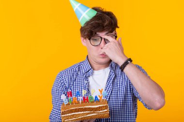 Sarı bir arka plan üzerinde poz mutlu bir doğum günü pastası tutan pozitif genç adam.