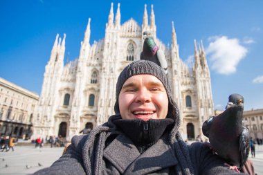 Kış seyahat, tatil ve kuşlar kavramı - yakışıklı erkek turist Milano'da ünlü Duomo Katedrali önünde selfie fotoğraf yapma komik güvercinler ile.