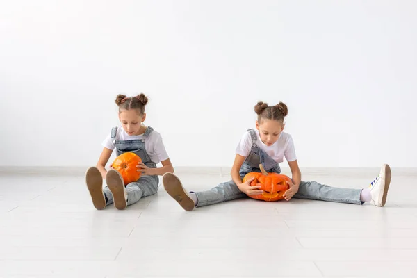 Feliz Halloween, vacaciones y concepto de la infancia - Lindas hermanas gemelas niñas con una calabaza Jack-o-lantern divertirse mientras pasa tiempo en el interior — Foto de Stock