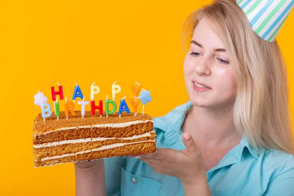Wakacje i zabawa cocept - zbliżenie pozytywne młoda kobieta gospodarstwa szczęśliwy tort urodzinowy pozowanie na żółtym tle. — Zdjęcie stockowe
