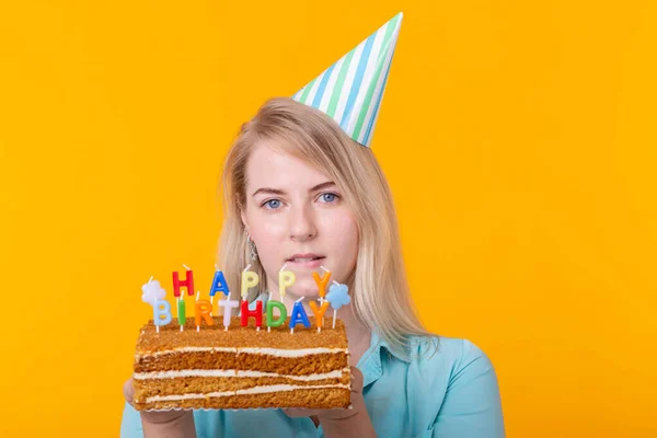 Ünnepek és party cocept - Pozitív fiatal nő kezében egy boldog születésnapi torta pózol sárga alapon, közelkép. — Stock Fotó