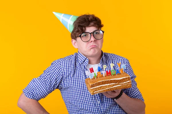 Positivo ragazzo divertente con un cappello e una torta fatta in casa nelle sue mani in posa su uno sfondo giallo. Anniversario e concetto di compleanno . — Foto Stock