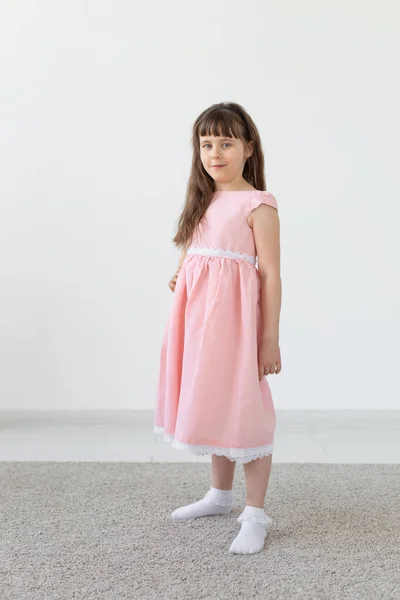 Belle petite fille brune dans une robe rose posant sur un fond blanc. Le concept d'enfants mignons. Espace de copie — Photo