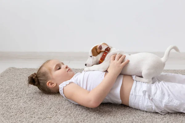 people, children and pets concept - little kid girl lying on the floor with cute puppy Jack Russell Terrier