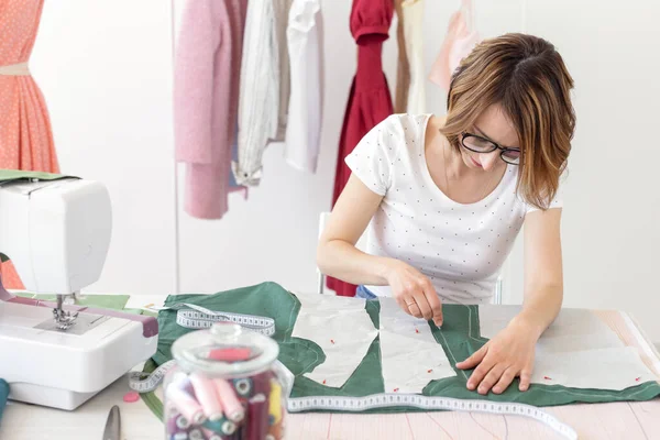 Positive young pretty girl seamstress designer working on a new project while sitting at her desk with a sewing machine in her workshop. Creative business concept. — Stock Photo, Image
