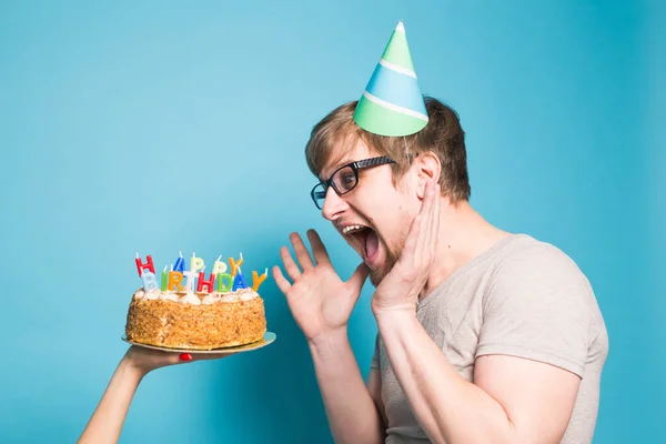 Engraçado jovem louco em um chapéu de papel de saudação quer morder um pedaço de bolo de parabéns. Conceito de brincadeira e cumprimentos de aniversário. Espaço de cópia — Fotografia de Stock