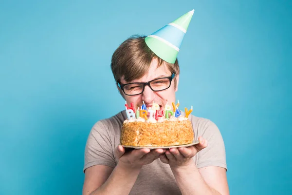 Divertente giovane pazzo in un cappello di carta augurale vuole mordere un pezzo di torta di congratulazioni. Concetto di scherzare e auguri di compleanno. Copia spazio — Foto Stock