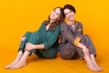 Renkli pijama giyen iki güzel genç kızın portresi sarı arka planda yatıya kalırken eğleniyorlar. Pijama partisi ve parti konsepti