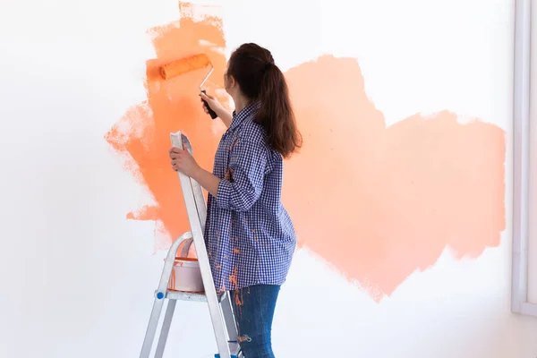 Bella pittura femminile la parete con rullo di vernice. Ritratto di una giovane bella donna che dipinge un muro nel suo nuovo appartamento. Concetto di ristrutturazione e ristrutturazione. Copia spazio . — Foto Stock