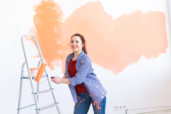 Bailando divertida mujer joven pintando la pared interior con rodillo de pintura en casa nueva. Una mujer con rodillo aplicando pintura en una pared . — Foto de Stock
