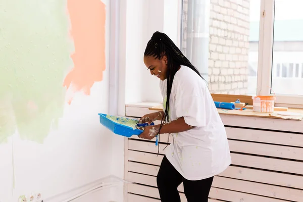 Riparazione nell'appartamento. Giovane donna felice dipinge il muro con vernice . — Foto Stock