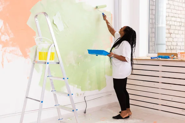Güzel afro-amerikalı kız duvarı boya rulosuyla boyuyor. Yeni dairesinde duvar boyayan güzel bir kadının portresi. Dekorasyon ve yenileme konsepti. — Stok fotoğraf