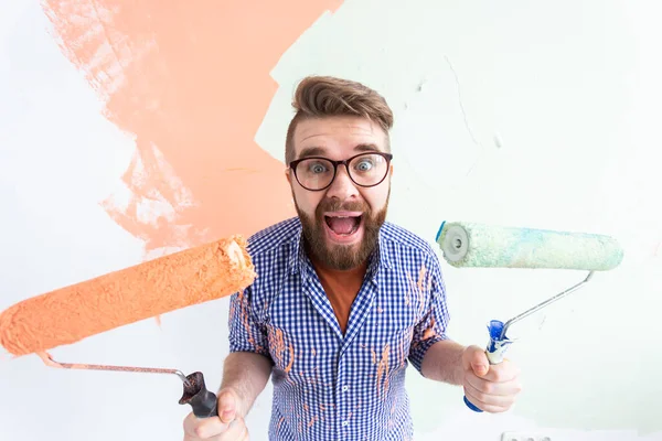 Funny man painting interior wall of home with paint roller. Redecoration, renovation, apartment repair and refreshment concept. — Stock Photo, Image