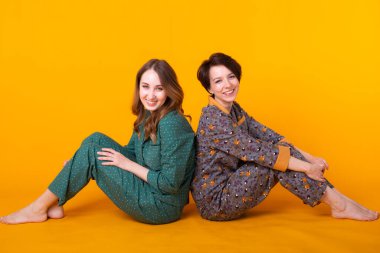 Renkli pijama giyen iki güzel genç kızın portresi sarı arka planda yatıya kalırken eğleniyorlar. Pijama partisi ve parti konsepti