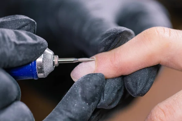 Manicure hardware in un salone di bellezza. manicure femminile sta applicando trapano lima elettrica per unghie per manicure sulle dita femminili. Manicure meccanica primo piano. Concetto cura del corpo. — Foto Stock