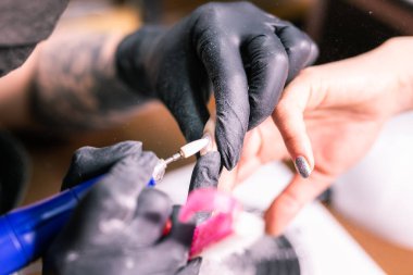 Jel cilasını çıkarmak için nalbur değirmenciliğine yakın çekim. Güzellik salonunda alet manikürü. Elektrikli çivi matkabı olan manikürcü eski jeli müşteri çivilerinden sökmüş. Eski Shillac 'ı değiştirme süreci.