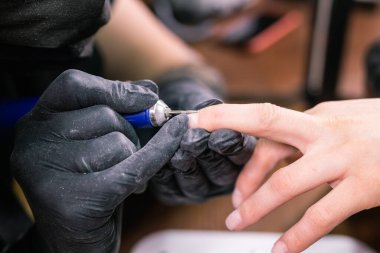 Manikürcü güzellik salonunda elektrikli tırnak matkabı kullanıyor. Mükemmel çivi manikür işlemi patlayan uçan enkazlarla kapatılır..