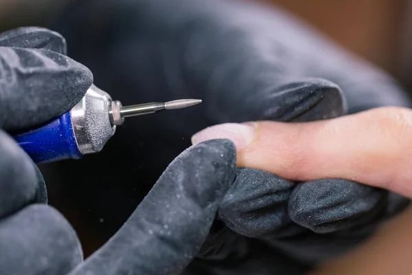 Manicurist use electric nail file drill in beauty salon. Perfect nails manicure process close up with burst flying debris.