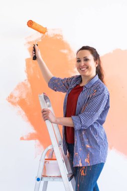 Evin içini boyayan gülümseyen kadın. Yenileme, onarım ve yeniden dekorasyon konsepti.