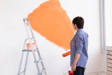 Oldukça gülümseyen orta yaşlı bir kadın evin içini boya rulosuyla boyuyor. Dekorasyon, yenileme, apartman onarımı ve ferahlatıcı konsept.