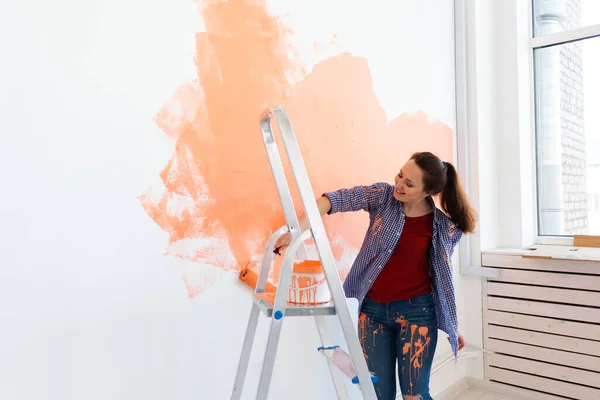 O femeie veselă pictează pereții unei case noi. Conceptul de renovare, reparare și redecorare . — Fotografie, imagine de stoc