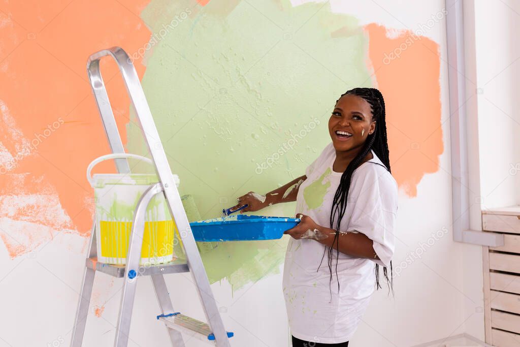 Young beautiful African American woman painting wall in her new apartment. Renovation and redecoration concept.