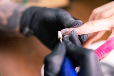 Jel cilasını çıkarmak için nalbur değirmenciliğine yakın çekim. Güzellik salonunda alet manikürü. Elektrikli çivi matkabı olan manikürcü eski jeli müşteri çivilerinden sökmüş. Eski Shillac 'ı değiştirme süreci.