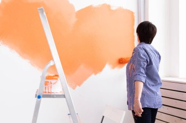 Orta yaşlı bir kadın yeni evin duvarlarını boyuyor. Yenileme, onarım ve yeniden dekorasyon konsepti.