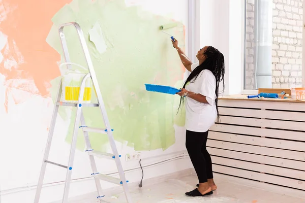 Felice donna afroamericana pittura muro nel suo nuovo appartamento. Concetto di ristrutturazione, ridecorazione e riparazione. — Foto Stock