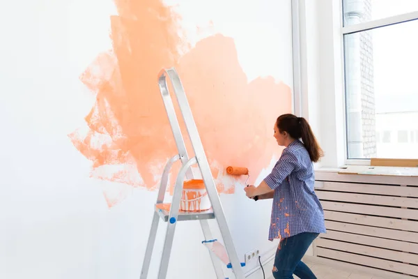 Mujer bastante sonriente pintando la pared interior del hogar con rodillo de pintura. Redecoración, renovación, reparación de apartamentos y concepto de refresco. — Foto de Stock