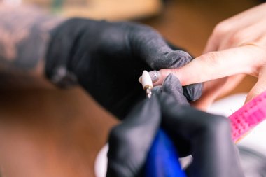 Manikürcü kadının yakın çekimi, manikür makinesi kullanarak müşterilerin tırnaklarındaki jöle parlatmasını kaldırıyor. Manikür ustası güzellik salonunda elektrikli tırnak matkabıyla çalışıyor. Donanım manikür süreci.