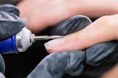 Güzellik salonunda hırdavatçı manikürü. Kadın manikürcü kadın parmaklarına manikür yapmak için elektrikli tırnak matkabı uyguluyor. Mekanik manikür yakın plan. Vücut bakımını kabul et.