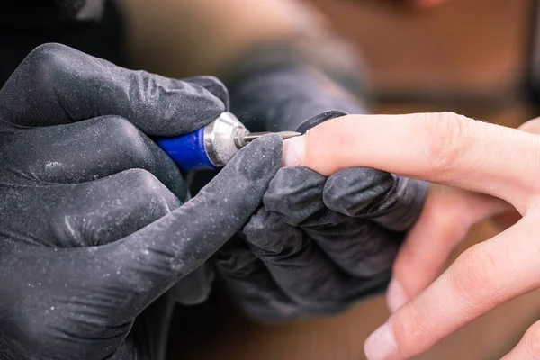 Manicure hardware in un salone di bellezza. manicure femminile sta applicando trapano lima elettrica per unghie per manicure sulle dita femminili. Manicure meccanica primo piano. Concetto cura del corpo. — Foto Stock