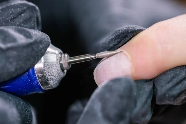 Woman use electric nail file drill in beauty salon. Nails manicure process in detail. Gel polish close-up concept.