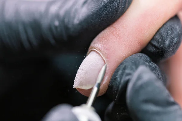 Primer plano de manicura de hardware en un salón de belleza. Manicura está aplicando taladro de lima de uñas eléctrica a la manicura en los dedos femeninos . —  Fotos de Stock