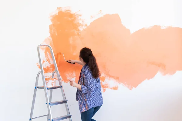 Smiling woman painting interior wall of home. Renovation, repair and redecoration concept.