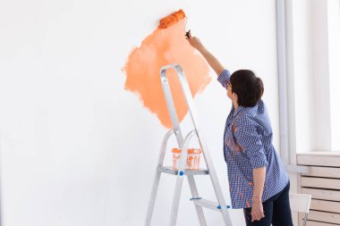 Yenileme, dekorasyon ve onarım konsepti - orta yaşlı kadın yeni evinde duvar boyuyor.