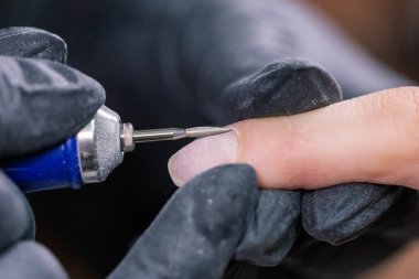 İşlem manikürü yakın çekim. Donanım manikürü için hazırlık. Lastik eldivenli güzellik uzmanı tırnak derisini kesip çivileri işliyor..