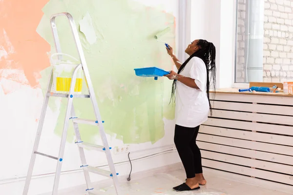 Giovane donna afro-americana felice pittura parete interna con rullo di vernice in nuova casa. Una donna con rullo che applica vernice su un muro. — Foto Stock