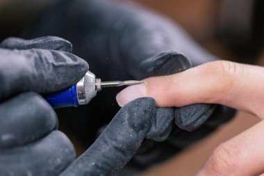 Kadın güzellik salonunda elektrikli tırnak matkabı kullanıyor. Manikür işlemini detaylıca yapıyor. Jel cilası yakın çekim konsepti.