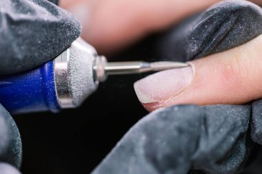 Güzellik salonundaki donanım manikürünü yakından çek. Manikürcü kadın parmaklarına manikür yapmak için elektrikli tırnak matkabı uyguluyor..