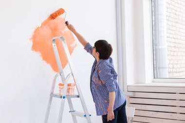 Yeni evin iç duvarlarını boyayan mutlu orta yaşlı kadın. Dekorasyon, yenileme, apartman onarımı ve ferahlatıcı konsept.