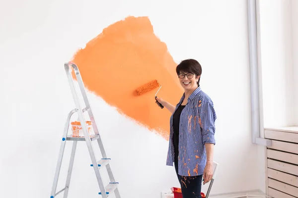 Happy middle-aged woman painting wall in her new apartment. Renovation, redecoration and repair concept.