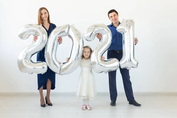 Młoda szczęśliwa rodzina matka i ojciec i córka stojący obok balonów w kształcie cyfr 2021 na białym tle. Nowy rok, Boże Narodzenie, wakacje — Zdjęcie stockowe