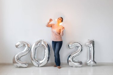 Yeni yıl kutlaması ve parti konsepti - Beyaz arka planda gümüş 2021 balonları yakınında maytaplı mutlu genç kadın.