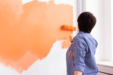 Orta yaşlı güzel bir kadın boya rulosuyla duvarı boyuyor. Yeni dairesinde duvar boyayan güzel bir kadının portresi. Dekorasyon ve yenileme konsepti. Arka plan.